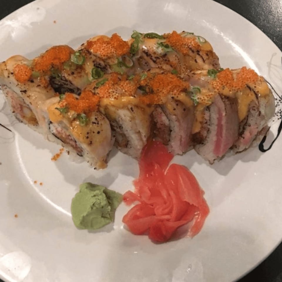 Sushi rolls topped with orange roe and green onions, served with wasabi and pickled ginger.
