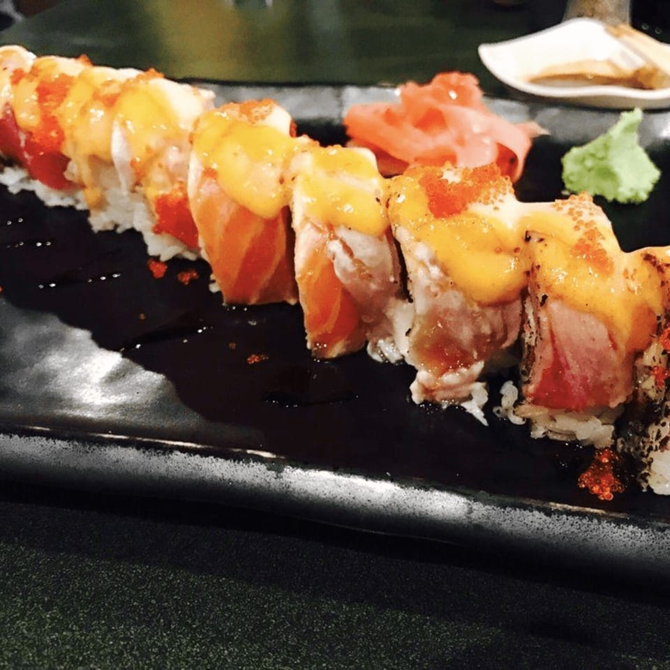 A long plate of Tokyo Dori sushi rolls topped with sauce and roe, with ginger and wasabi.