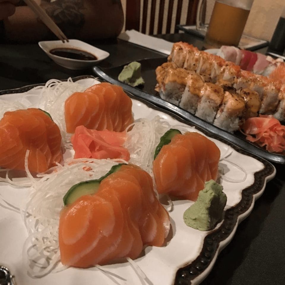 Plates of salmon sashimi, sushi rolls, and wasabi on a dark table at Tokyo Dori.