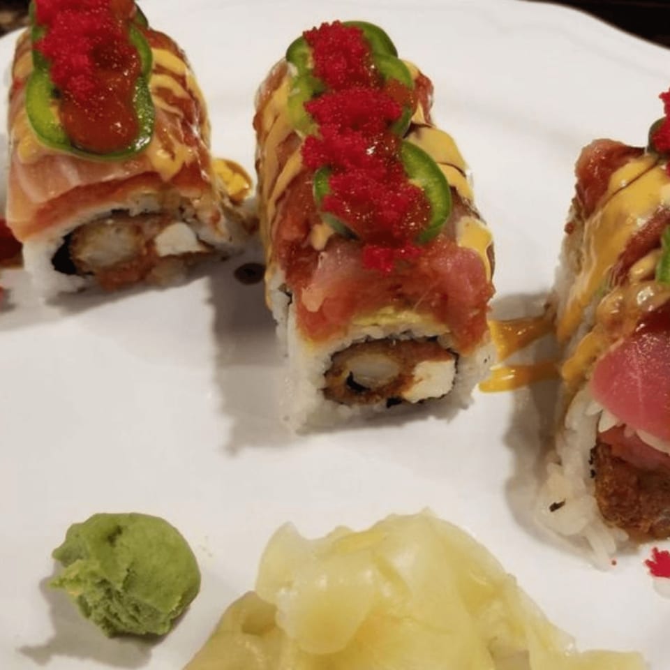 Three sushi rolls topped with salmon, roe, jalapeños, and sauce, with wasabi and ginger.